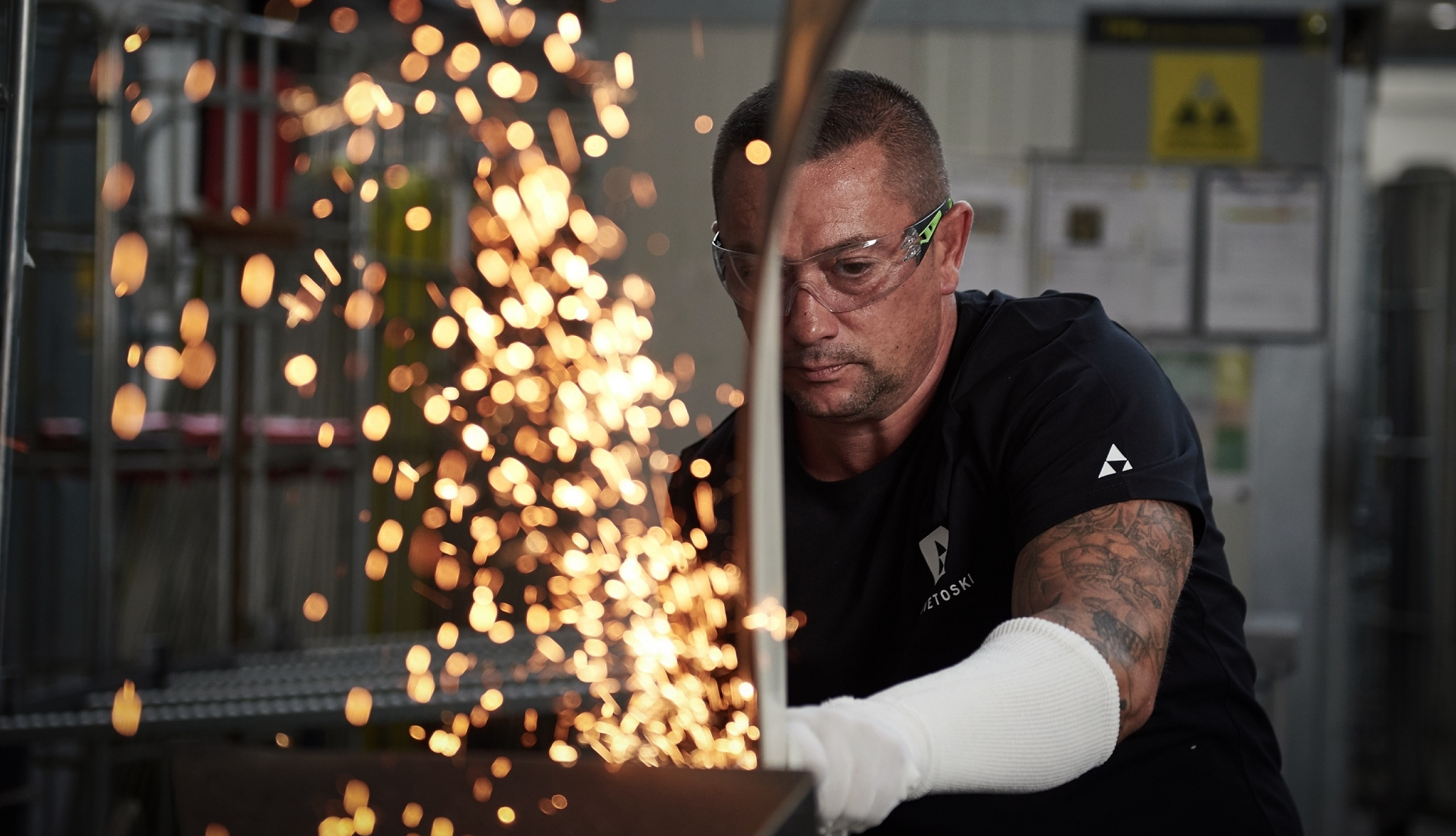 Produktionsmitarbeiter mit Schutzbrille schleift die Kanten eines Skis, Funken sprühen